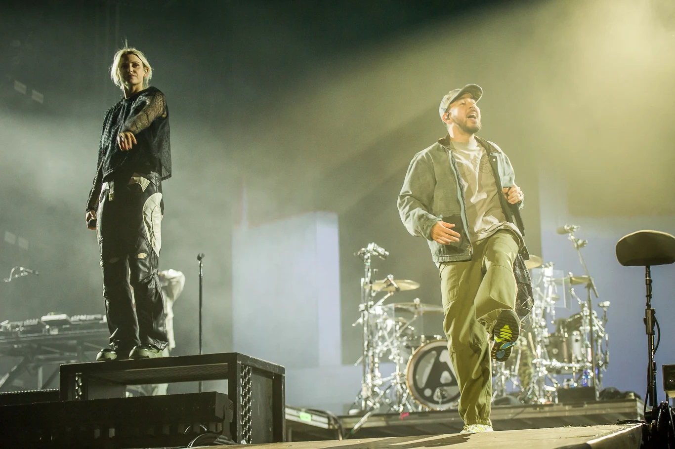 Open'er Festival 2025: Linkin Park Dwóch mężczyzn występuje na jasnej scenie koncertowej, jeden z nich stoi na podwyższeniu, w tle widać perkusję oraz inne instrumenty muzyczne, scena oświetlona jest kolorowymi światłami, a całość tworzy dynamiczny klimat muzycznego wydarzenia.