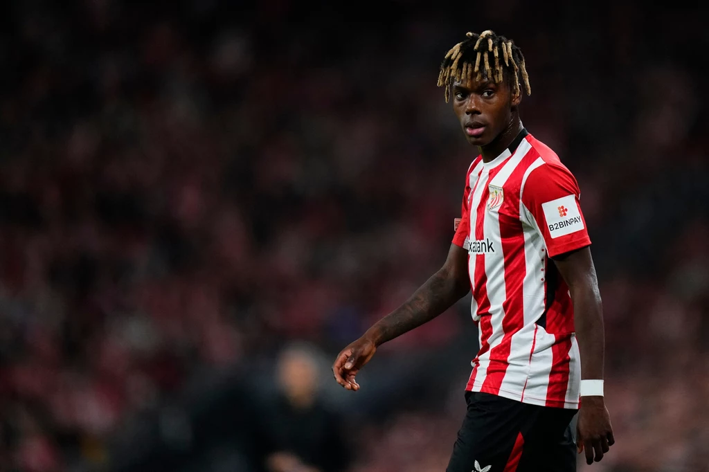 Nico Williams Piłkarz w stroju czerwono-białej drużyny podczas meczu na stadionie, widoczny intensywny wyraz twarzy sportowca oraz rozmyte tło trybun.