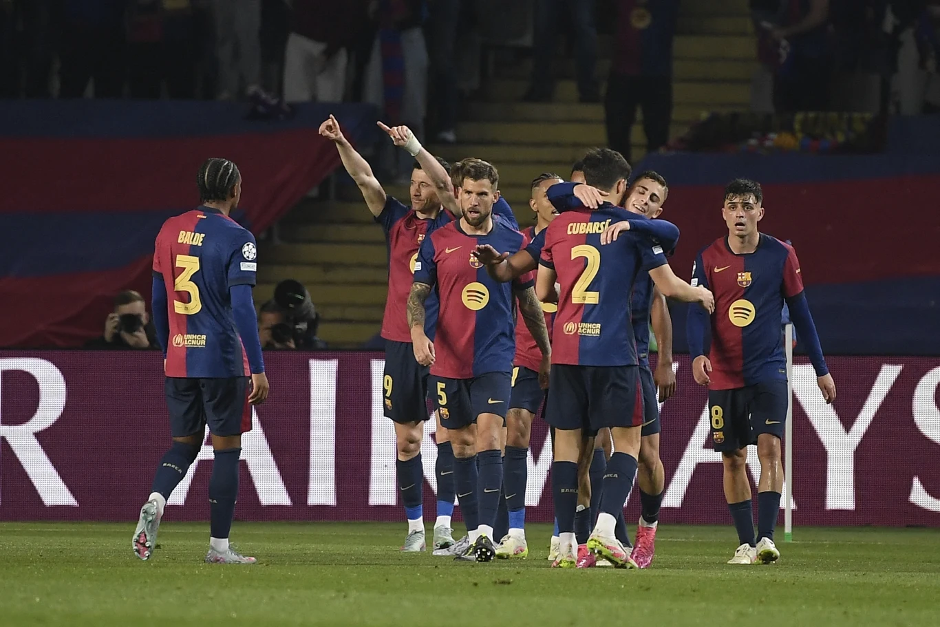 Piłkarze FC Barcelona Piłkarze drużyny FC Barcelona w oficjalnych strojach sportowych świętują bramkę podczas meczu na stadionie, kilku z nich przytula się i unosi ręce w geście radości, na trybunach widoczni kibice i klubowe barwy.