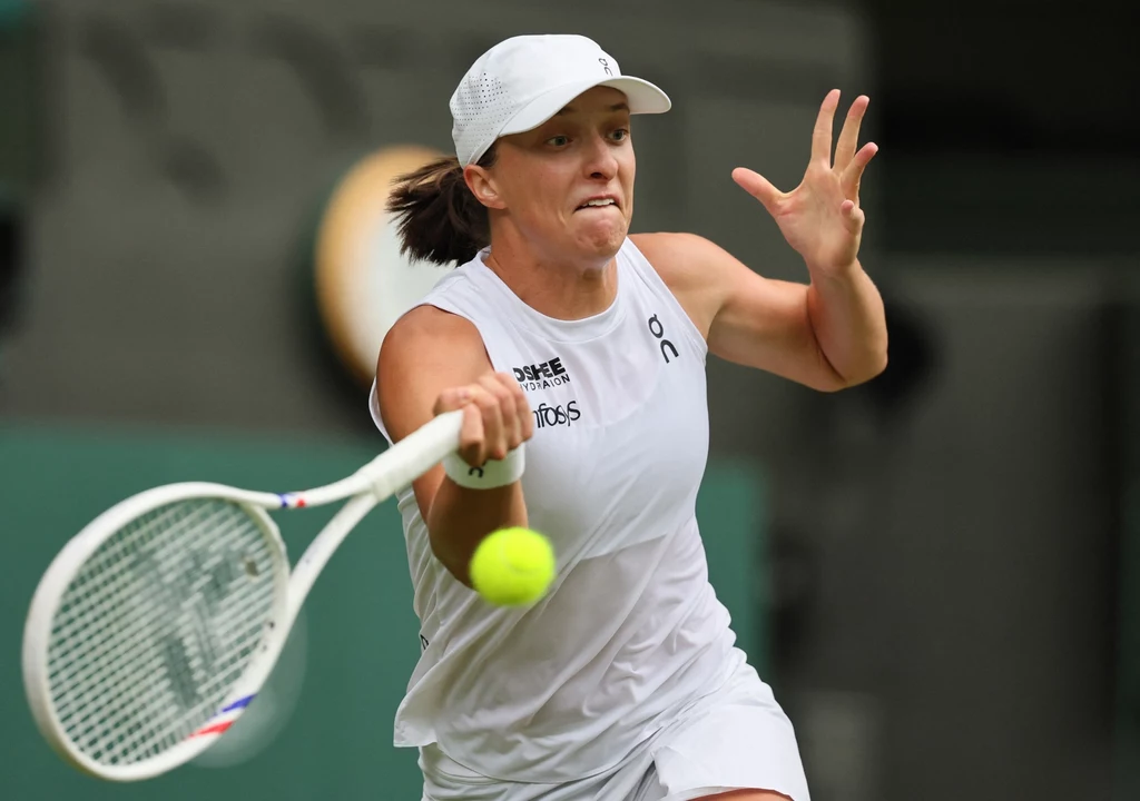 Iga Świątek w trakcie meczu Wimbledonu 2025 Tenisistka w białym stroju dynamicznie odbijająca piłkę rakietą na korcie tenisowym, skupienie i intensywność widoczne na jej twarzy.