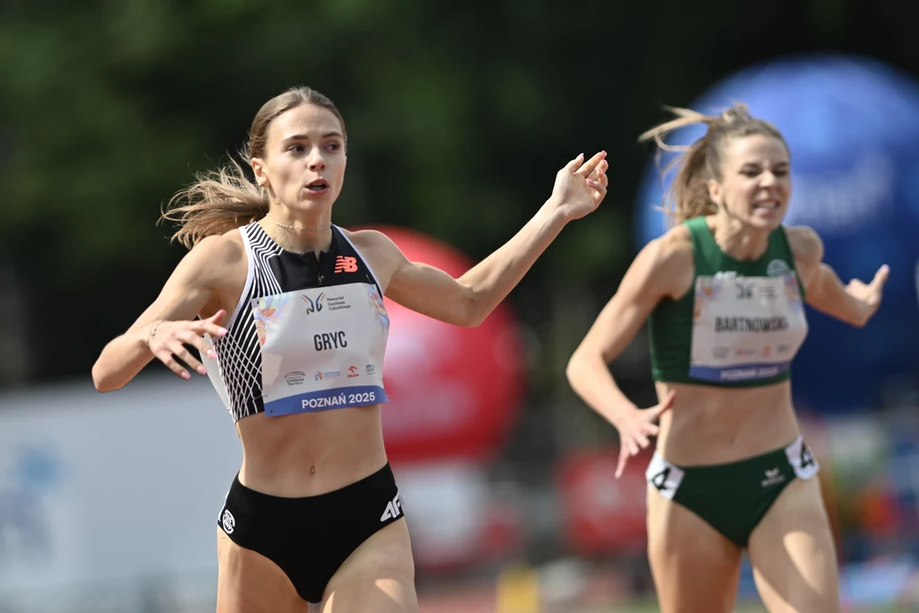 Dwie lekkoatletki walczące o zwycięstwo podczas biegu na stadionie, obie zawodniczki w sportowych strojach, z widocznymi numerami startowymi i nazwiskami.