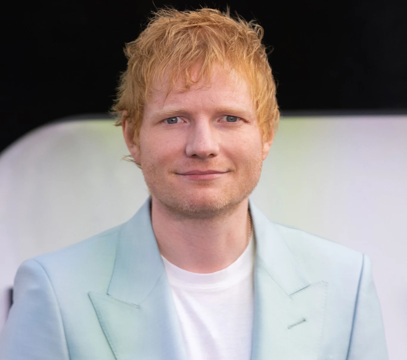 Ed Sheeran nagrał najpopularniejszą piosenkę dekady Mężczyzna o rudych włosach ubrany w jasnoniebieską marynarkę i białą koszulkę, uśmiechnięty, stoi na tle rozmytego jasnego tła.