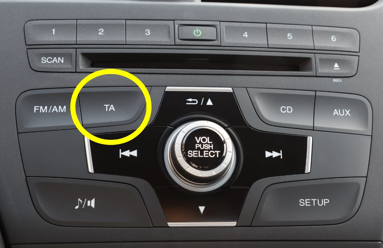 Do czego służy TA w samochodzie? Panel sterowania radia samochodowego z wyraźnie zaznaczonym przyciskiem TA i przyciskami opisanymi jako FM/AM, CD, AUX, SCAN, SETUP oraz pokrętłem głośności pośrodku.