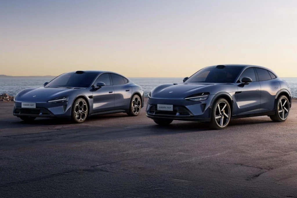Sedan SU7 cieszy się sporym zainteresowaniem. Założyciel Xiaomi zapewnia, że oba modele nie będą sobie szkodzić na rynku. Dwa nowoczesne elektryczne samochody sportowe ustawione obok siebie na wybrzeżu przy zachodzącym słońcu, na czystym asfalcie, z widocznym morzem i horyzontem w tle.
