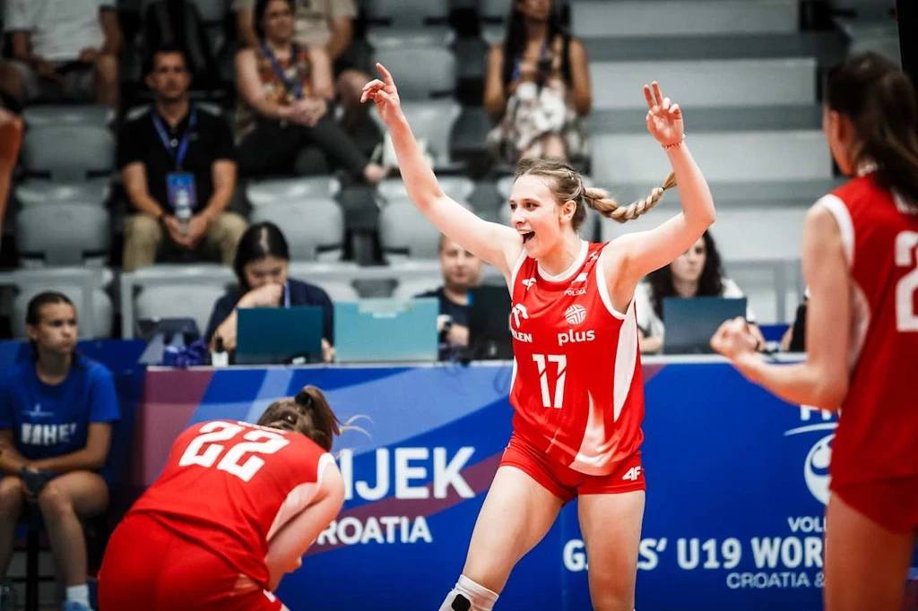 Zawodniczka siatkarskiej reprezentacji Polski w czerwonym stroju świętuje zdobycie punktu, otoczona przez koleżanki z drużyny podczas meczu, na trybunach widoczna publiczność i obsługa techniczna.