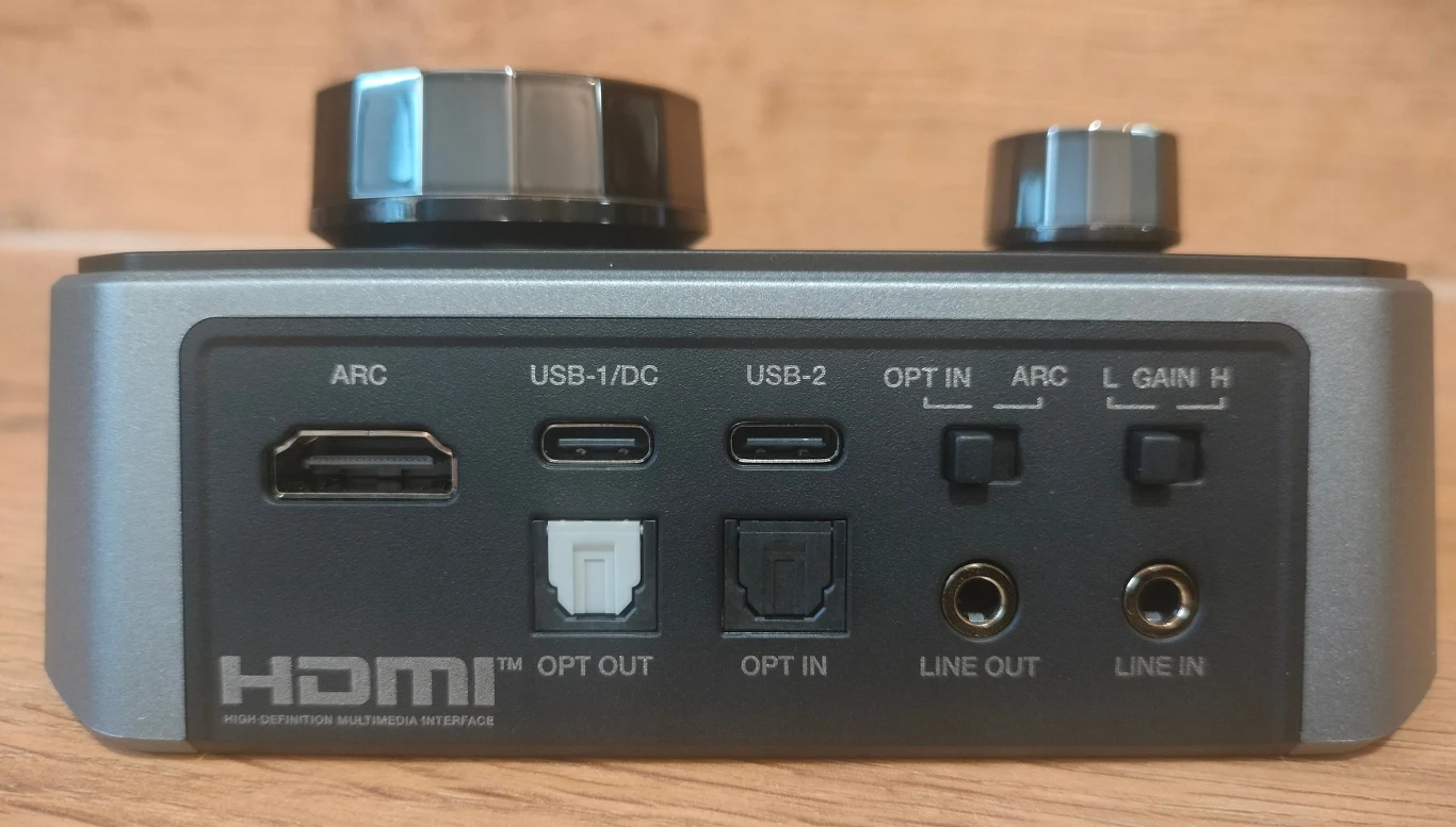 Creative Sound Blaster G8 Panel tylni urządzenia audio z widocznymi złączami HDMI, USB-C, optycznymi wejściami i wyjściami, wejściami liniowymi i pokrętłami regulacji, na tle drewnianym.