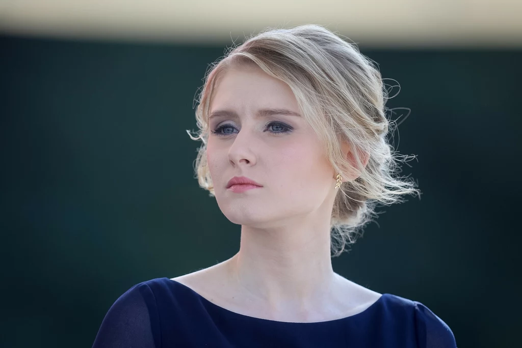 Kinga Duda w 2020 r. Młoda kobieta o jasnych włosach upiętych w elegancki kok, ubrana w granatową suknię, patrzy w dal z poważnym wyrazem twarzy, na tle rozmytego, ciemnego tła.