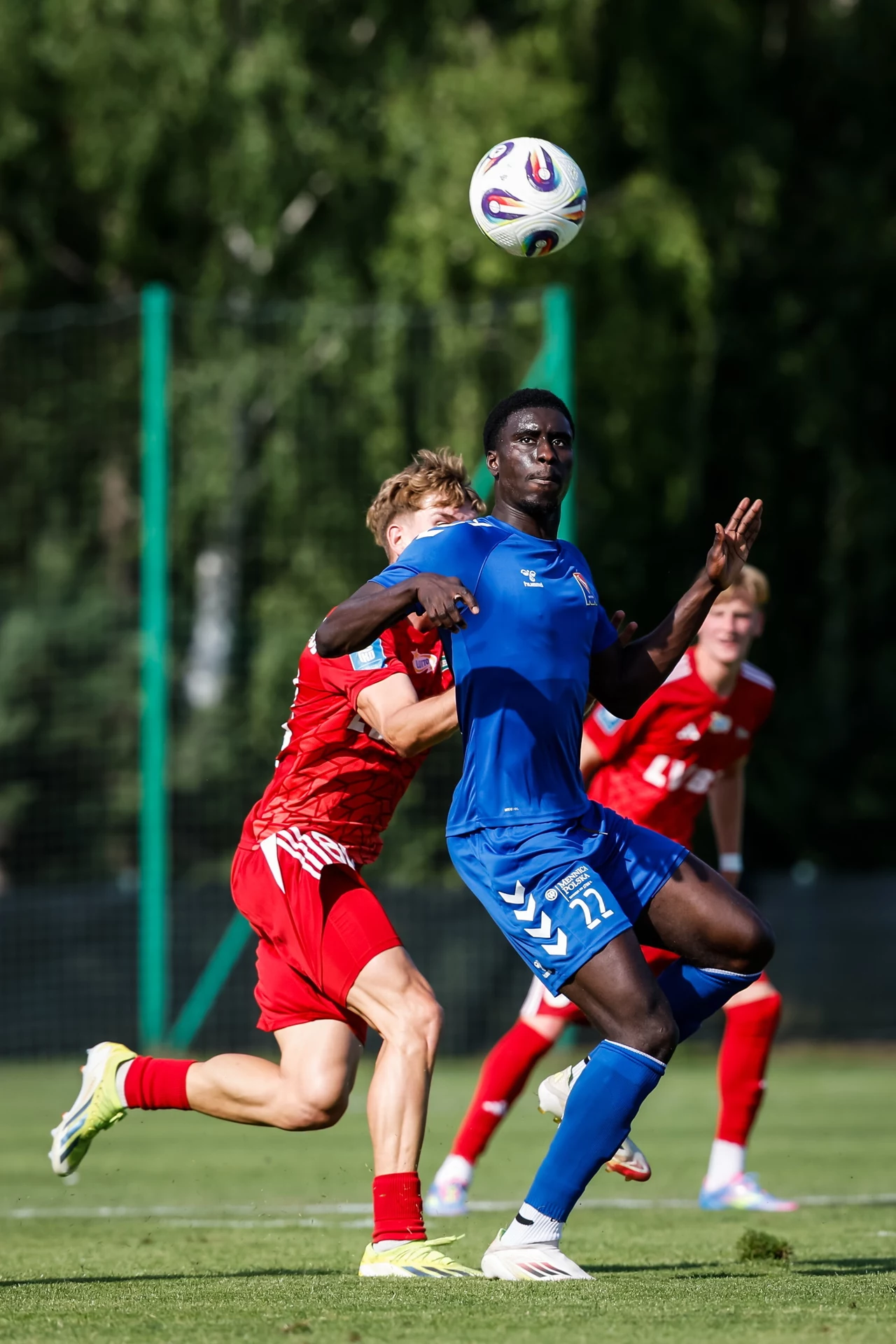 Kadr z sobotniego meczu Motor Lublin - Lechia Gdańsk. Zdjęcie wykonano legalnie Dwóch piłkarzy walczy o piłkę w powietrzu podczas meczu, zawodnik w niebieskim stroju skacze do piłki, obok niego znajduje się przeciwnik w czerwonym stroju, w tle widać boisko i innych graczy.