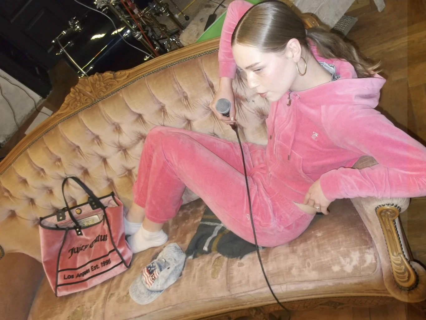 AJLA wydała album "Ala17 EP" Młoda kobieta w różowym welurowym dresie z mikrofonem w dłoni siedzi na zabytkowej, beżowej sofie, obok niej znajduje się stylowa torba Juicy Couture, na podłodze leży stopa w skarpetkach i klapkach, a w tle widać elementy perkusji.