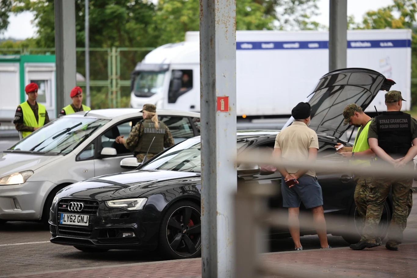 Straż Graniczna informuje o działaniach na granicy polsko-litewskiej Funkcjonariusze Straży Granicznej ubrani w mundury i kamizelki odblaskowe przeprowadzają kontrolę dwóch pojazdów osobowych, przy jednym z samochodów stoi kilku żołnierzy oraz kierowca prezentujący dokumenty.