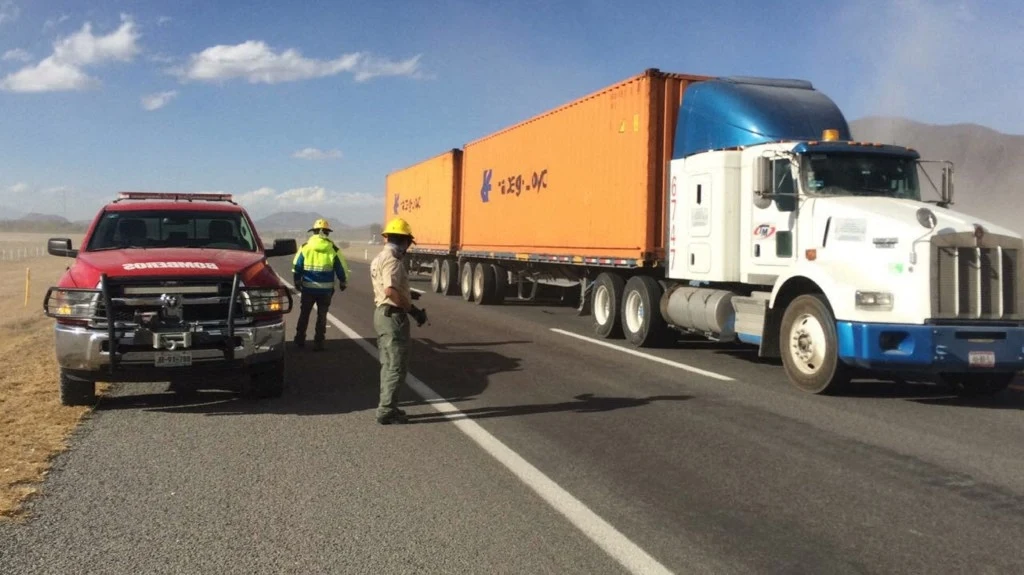 Do napadu doszło na jednej z meksykańskich autostrad (zdjęcie ilustracyjne) Policjanci oraz pojazd służbowy stoją na poboczu autostrady obok dużej ciężarówki z pomarańczową naczepą, ruch na drodze został zatrzymany, a obecność służb sugeruje kontrolę lub interwencję w sytuacji kryzysowej.