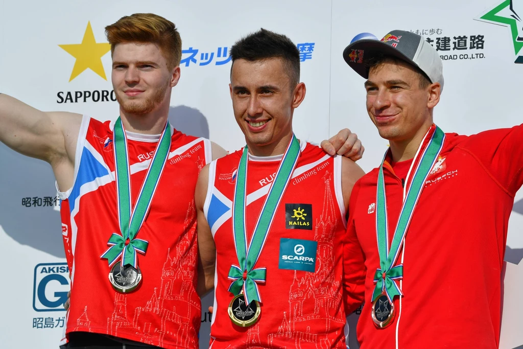Marcin Dzieński (pierwszy od prawej) na podium zawodów PŚ w Tokio w 2018 roku Trzech młodych mężczyzn w sportowych strojach z medalami na szyi pozuje razem na podium podczas ceremonii wręczenia nagród