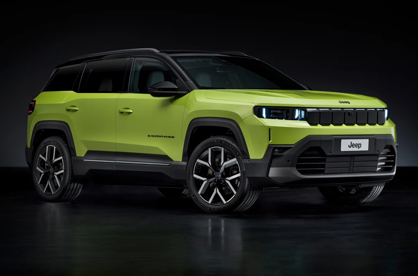Nowy Compass w wersji First Edition. Odświeżony design i napędy hybrydowe oraz elektryczne mają przyciągnąć nowych klientów. Jasnozielony SUV Jeep Compass ustawiony w dobrze oświetlonym studiu, widoczny z boku i lekko z przodu, podkreślone nowoczesne linie nadwozia oraz charakterystyczna przednia osłona chłodnicy.