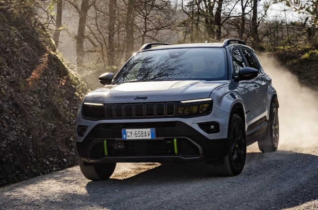 Avenger 4xe w wersji The North Face produkowany jest w Polsce. Powstanie tylko 4806 sztuk. SUV marki Jeep porusza się dynamicznie po szutrowej drodze w otoczeniu drzew i unoszącego się kurzu, światło słoneczne przebija się przez gałęzie, podkreślając sylwetkę pojazdu.