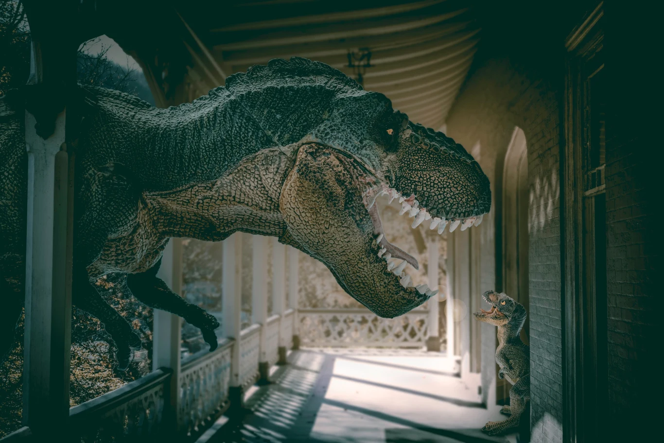 Dwa dinozaury, jeden duży i jeden mały, znajdują się na werandzie budynku, zwrócone są ku sobie, większy dinozaur dominuje przestrzeń swoją posturą, natomiast mniejszy stoi naprzeciwko niego.