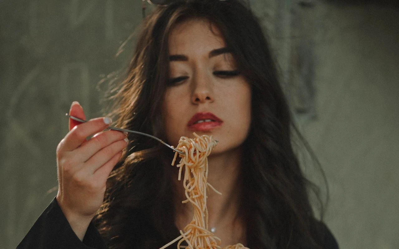 Włoszki zdradzają sekret urody. Zdziwisz się, jak niewiele trzeba Kobieta o długich, ciemnych włosach trzyma widelec z porcją makaronu spaghetti, patrząc na jedzenie w skupieniu, tło jest neutralne i nie zawiera istotnych detali.