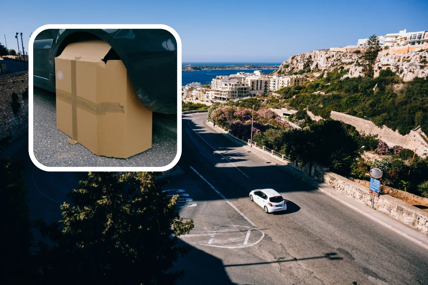 Kierowcy zasłaniają koła kartonem i twierdzą, że to ma sens. Białe auto jedzie słoneczną ulicą pośród skał i roślinności, w tle widoczne nowoczesne budynki oraz morze, a w lewym górnym rogu umieszczony jest karton ustawiony przy kole samochodu.