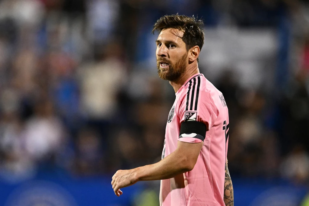 Lionel Messi Piłkarz w różowej koszulce z opaską kapitana na ramieniu, w tle rozmyta publiczność i stadionowe światła.