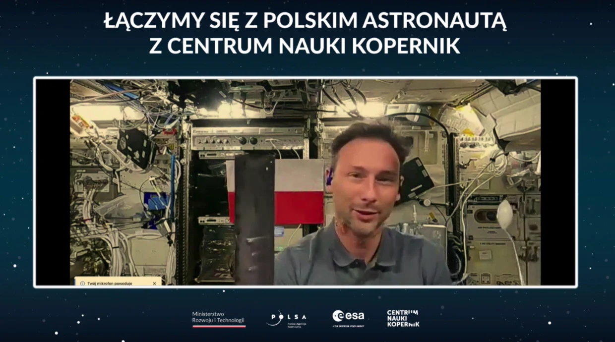 Sławosz Uznański-Wiśniewski podczas łączenia z Centrum Nauki Kopernik Polski astronauta podczas wideorozmowy z Centrum Nauki Kopernik znajduje się w otoczeniu zaawansowanego sprzętu kosmicznego oraz polskiej flagi, w tle wnętrze stacji kosmicznej.