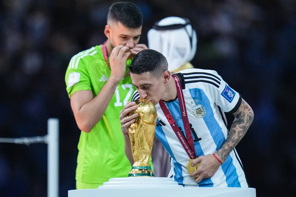 Angel Di Maria w 2022 roku w Katarze sięgnął po upragnione mistrzostwo świata Argentyński piłkarz całuje Puchar Świata FIFA, obok stoi inny zawodnik w zielonym stroju z medalem, który również celebruje zwycięstwo.