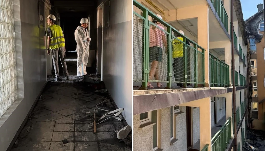 Skutki pożaru kompleksu mieszkalnego w Ząbkach Dwóch mężczyzn w kaskach ochronnych i odzieży roboczej sprawdzających uszkodzony, zadymiony korytarz budynku, po prawej stronie widoczni ludzie oraz inspektor lub policjant na zewnętrznym balkonie tej samej nieruchomości.