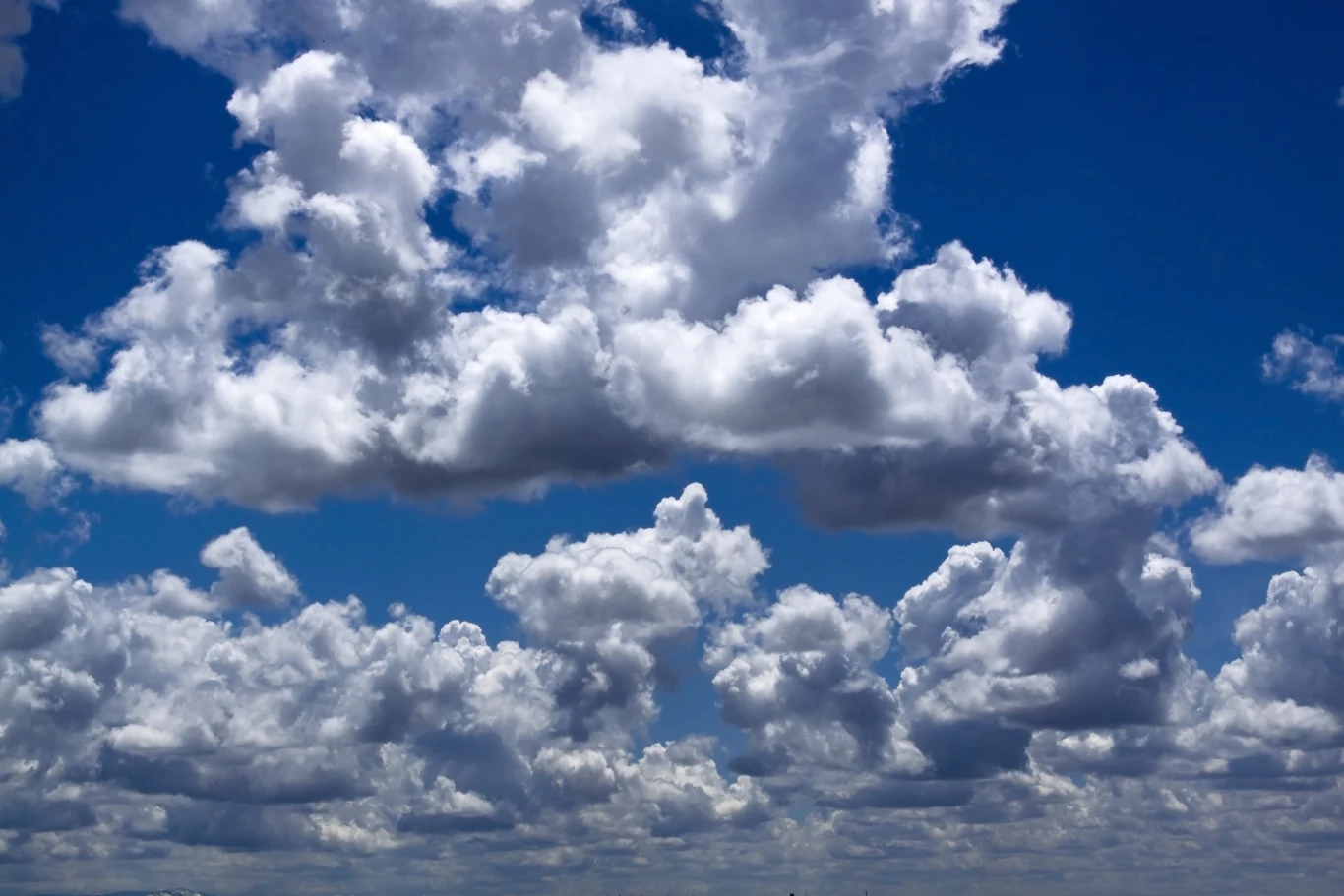 Białe, puszyste chmury unoszące się na tle głębokiego, niebieskiego nieba w pogodny dzień.