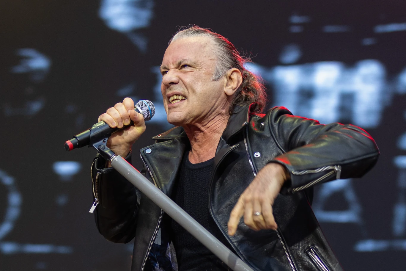 Bruce Dickinson (Iron Maiden) w akcji - Londyn, 28 czerwca 2025 r. Mężczyzna w skórzanej kurtce śpiewający energicznie do mikrofonu na scenie, wyrażający emocje poprzez ekspresyjną mimikę i gestykulację, w tle nieostre światła sceniczne.