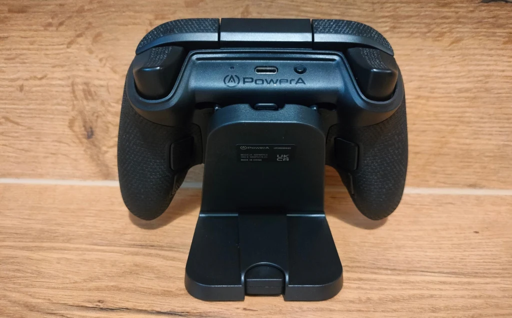 Pad do gier marki PowerA umieszczony na ładowarce, sfotografowany z tyłu, leży na drewnianej powierzchni.