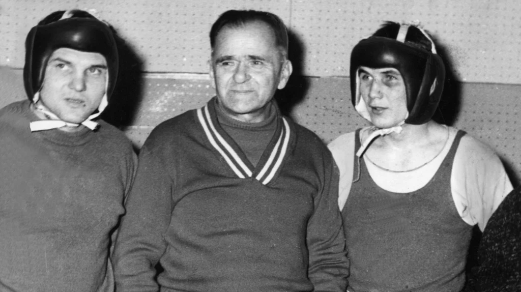 Feliks Stamm (w środku) z Jerzym Kulejem (po lewej) i Janem Gałązką Trzech mężczyzn, z których dwóch ubranych jest w sportowe stroje bokserskie i ochraniacze na głowie, stoi obok siebie w sali treningowej, środkowy mężczyzna ubrany w sweter pełni najwyraźniej funkcję trenera.