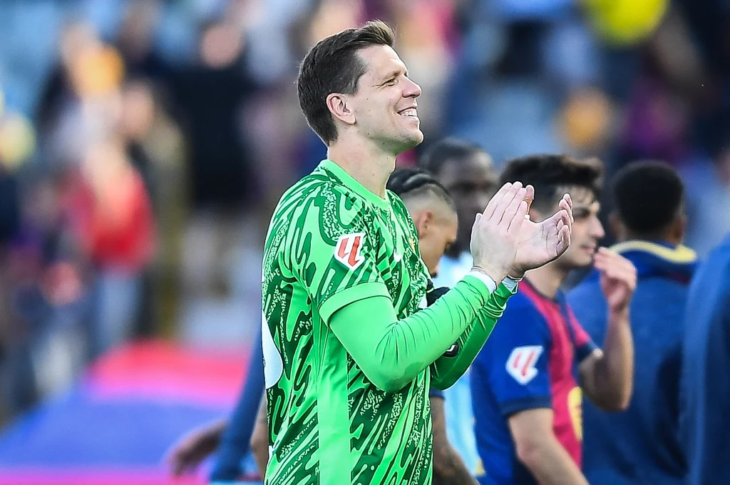 Wojciech Szczęsny w barwach FC Barcelona piłkarz w zielonym stroju bramkarza klaszcze, stojąc pośród innych zawodników na boisku, w tle rozmazana widownia trybun