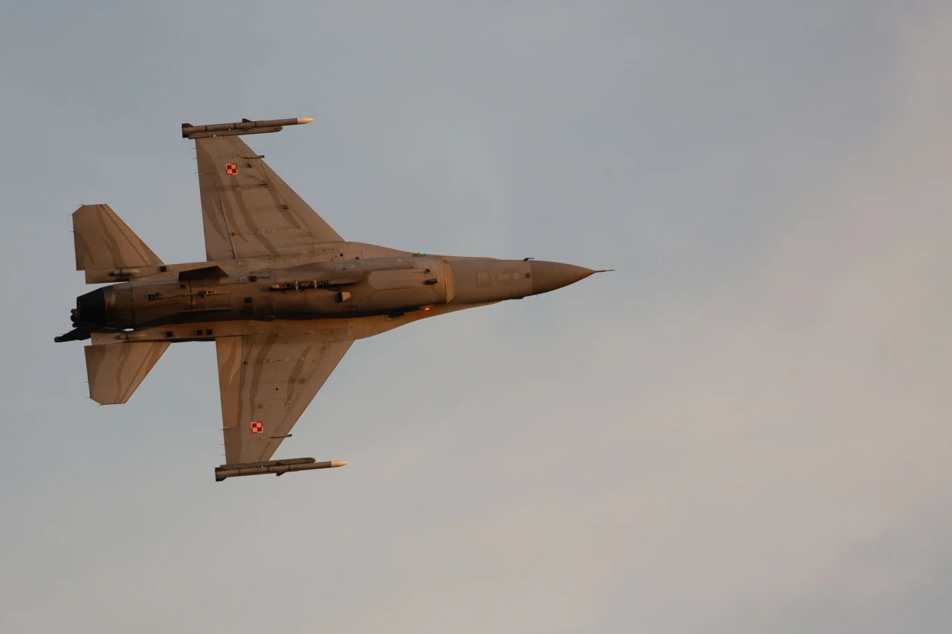 Polska poderwała myśliwce. "Monitorujemy sytuację" Myśliwiec F-16 z polskimi oznaczeniami w locie na tle jasnego nieba.