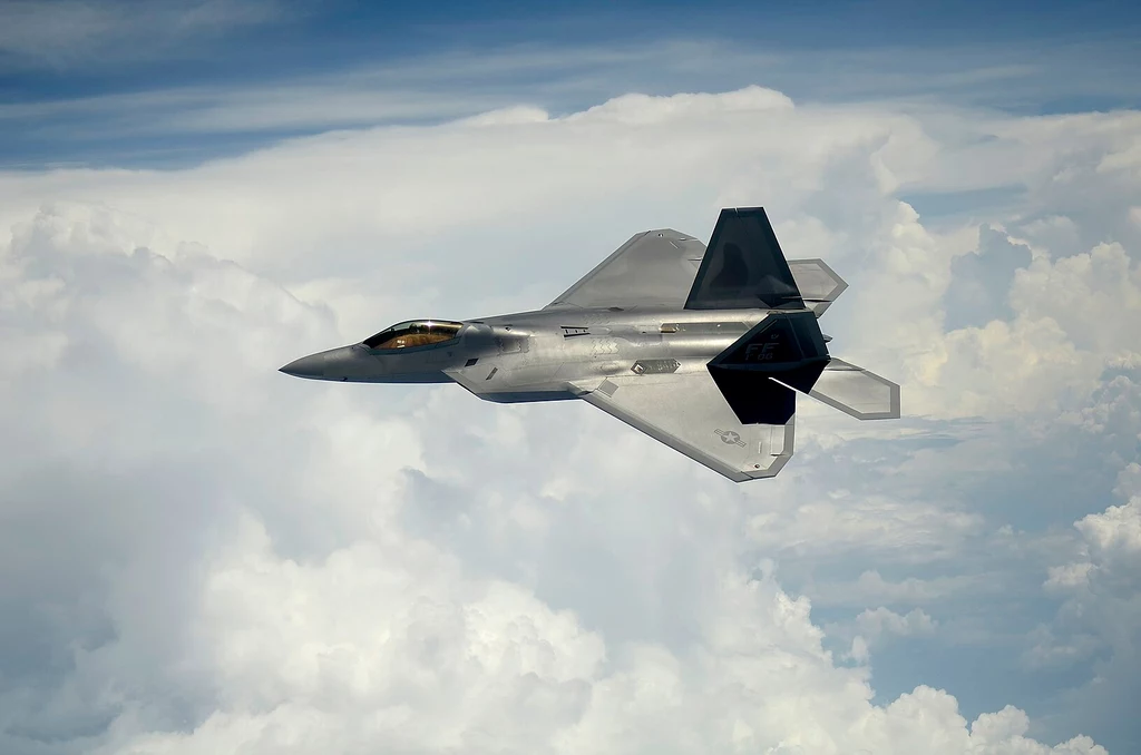 Myśliwiec F-22 Raptor Myśliwiec odrzutowy F-22 Raptor leci ponad białymi chmurami na tle błękitnego nieba.