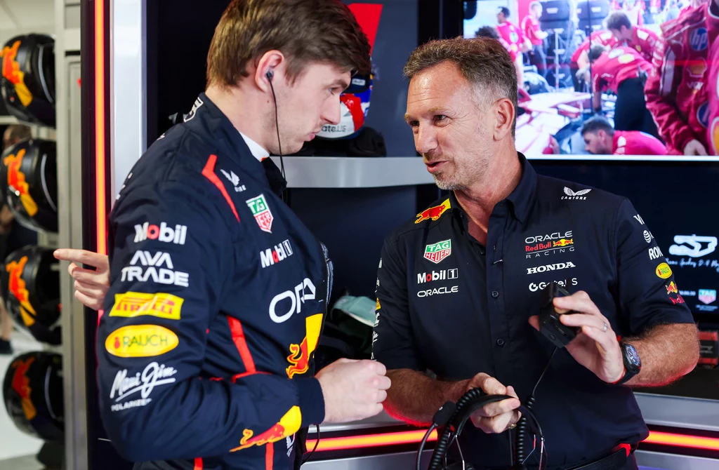 Christian Horner po latach odchodzi z Red Bull Racing Dwóch mężczyzn w strojach zespołu wyścigowego Red Bull rozmawia ze sobą w garażu, jeden z nich trzyma słuchawki, a w tle widoczni są inni członkowie zespołu oraz hełmy wyścigowe.