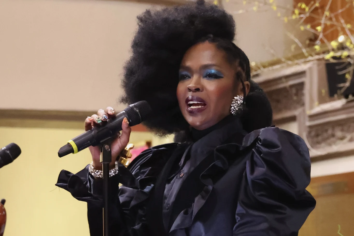 Lauryn Hill znalazła się w ogniu krytyki po sporym opóźnieniu koncertu Kobieta o efektownej fryzurze afro i mocnym makijażu śpiewa do mikrofonu, ubrana w elegancką, ciemną suknię z ozdobami na rękach i uszach, w tle widoczne są dekoracje i elementy architektury wnętrza.