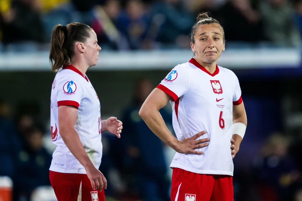 Polska - Szwecja na Euro 2025 Dwie piłkarki reprezentacji Polski w białych koszulkach i czerwonych spodenkach stoją na boisku, jedna z nich z numerem 6 trzyma ręce na biodrach i ma wyraz twarzy sugerujący zamyślenie lub rozczarowanie.
