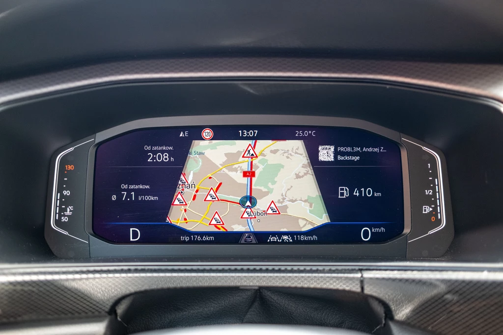 Cyfrowy wyświetlacz samochodu z wbudowaną nawigacją GPS pokazuje mapę z licznymi ostrzeżeniami drogowymi oraz informacjami o trasie, prędkości i stanie paliwa.