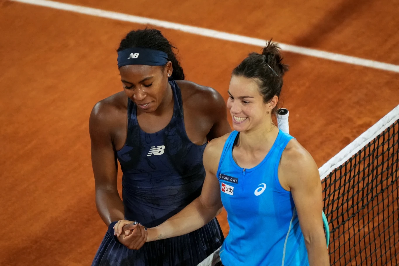 Lois Boisson i Coco Gauff po półfinale Roland Garrosa w 2025 roku Dwie tenisistki przy siatce na korcie ziemnym, ubrane w sportowe stroje, jedna obejmuje drugą w geście sportowej życzliwości, obie uśmiechnięte, w tle widoczna pomarańczowa nawierzchnia kortu.