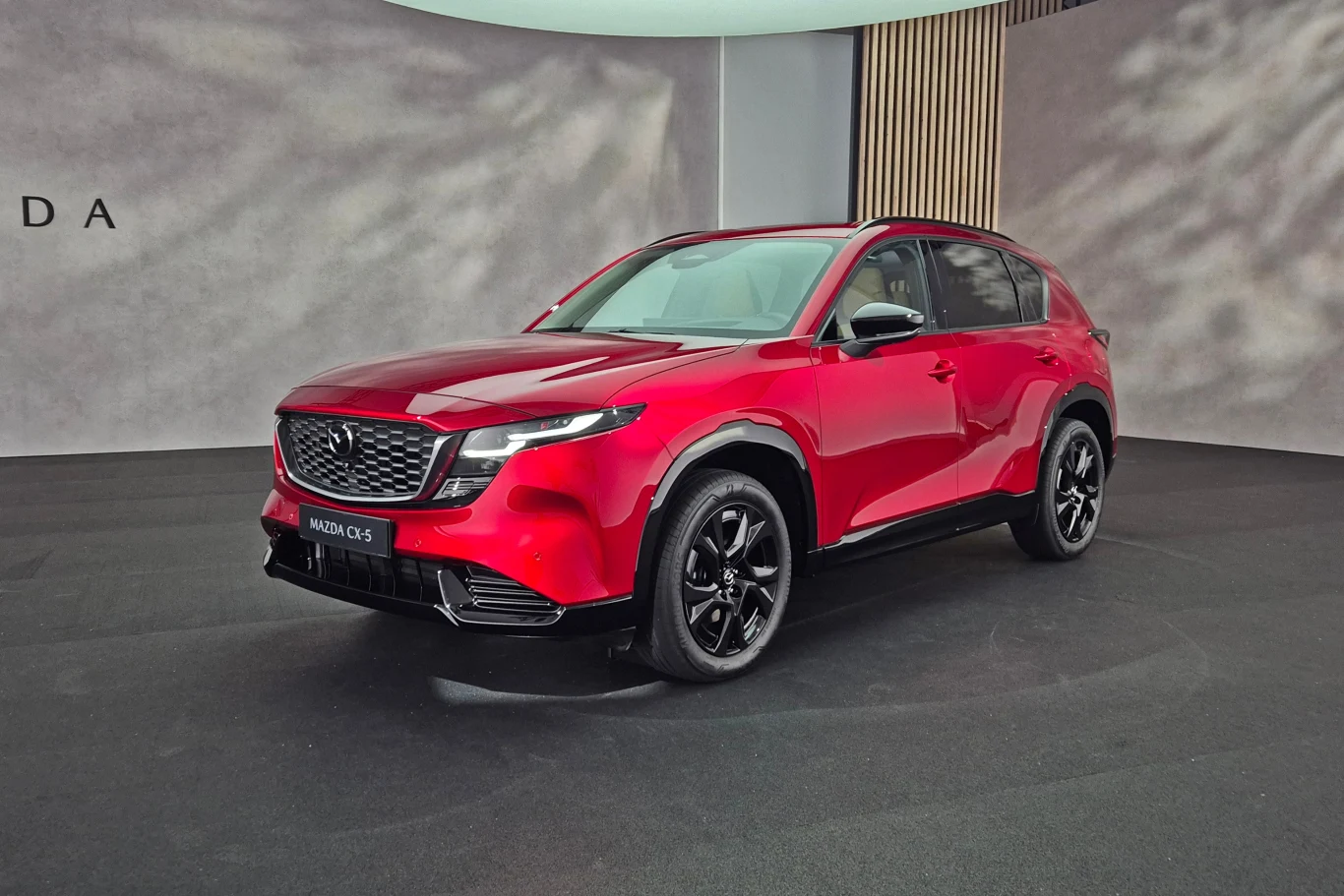 Czerwony SUV marki Mazda CX-5, nowoczesna stylistyka nadwozia, eleganckie czarne felgi, jasne oświetlenie wystawowe, minimalistyczne tło z logotypem marki.