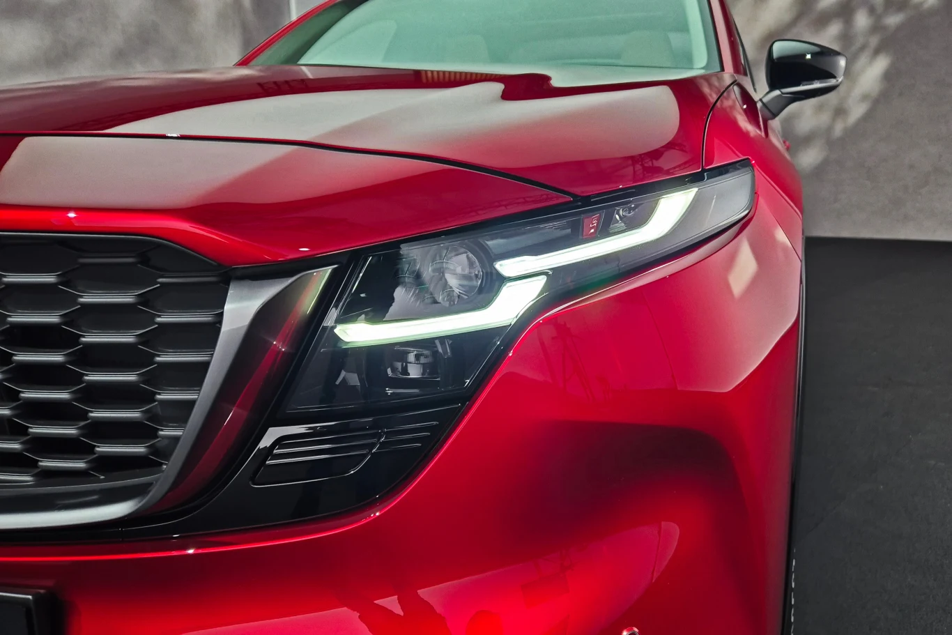 Reflektory CX-5 wyglądają na wąskie jak w poprzedniku, ale tak naprawdę mają kształt litery L Zbliżenie na przednią część czerwonego samochodu z nowoczesnym reflektorem LED i wyrazistą atrapą chłodnicy