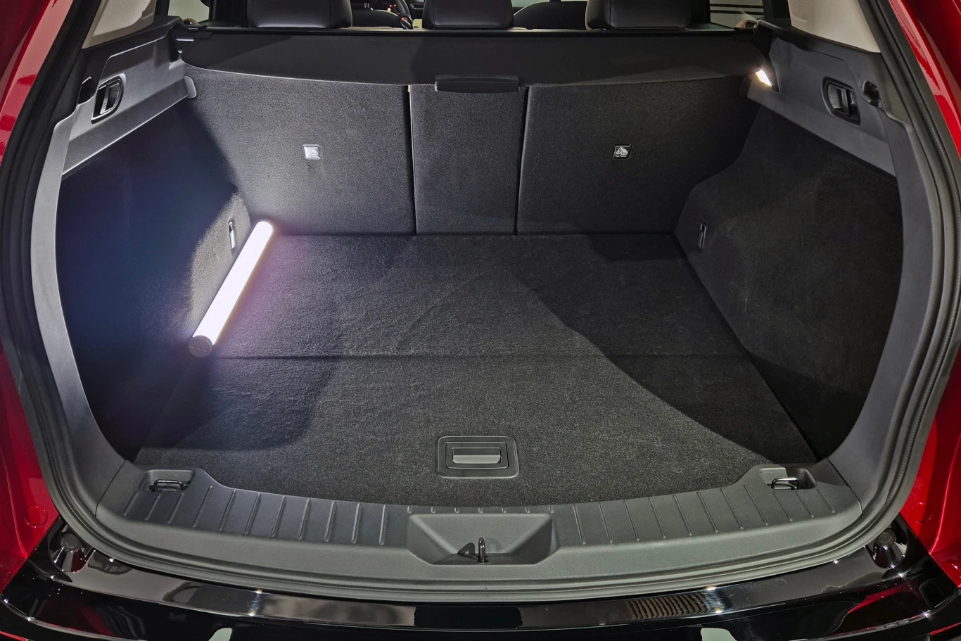 Bagażnik CX-5 ma 581 l, ale pod warunkiem, że liczymy także przestrzeń pod podłogą Przestronny, czysty bagażnik samochodu osobowego z rozłożonymi tylnymi siedzeniami i włączonym oświetleniem po lewej stronie.