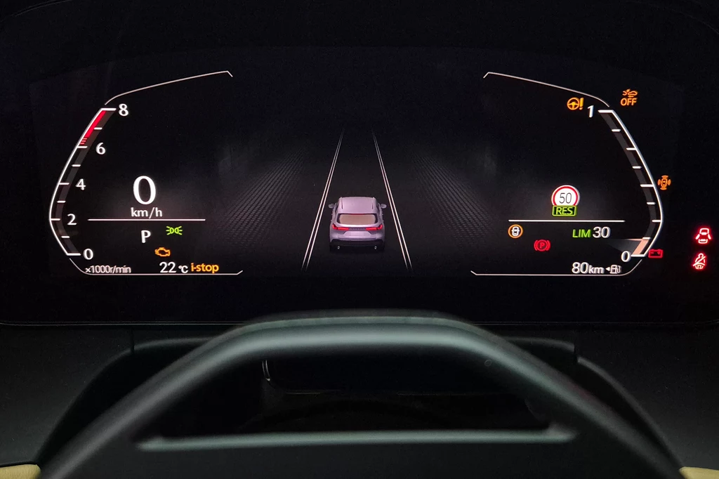 Nowe cyfrowe zegary w CX-5 mają kilka widoków, ale nadal ich możliwości na tle niektórych konkurentów są wyraźnie ograniczone Cyfrowy kokpit samochodu z widocznym prędkościomierzem, obrotomierzem, informacjami o stanie pojazdu oraz przedstawieniem samochodu na ekranie centralnym, otoczonego wskaźnikami i ikonami systemów bezpieczeństwa oraz ostrzeżeniami.
