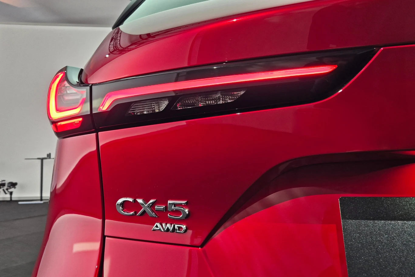 Mazda CX-5 dostępna jest z napędem na przód lub AWD Czerwony tył samochodu Mazda CX-5 z podświetlonym tylnym światłem i oznaczeniem AWD, ukazujący nowoczesny design i detale karoserii.