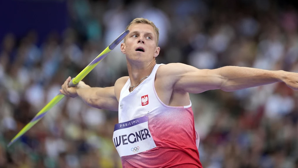 Sportowiec w stroju reprezentacji Polski rzuca oszczepem podczas zawodów lekkoatletycznych na stadionie, w tle rozmyta publiczność.