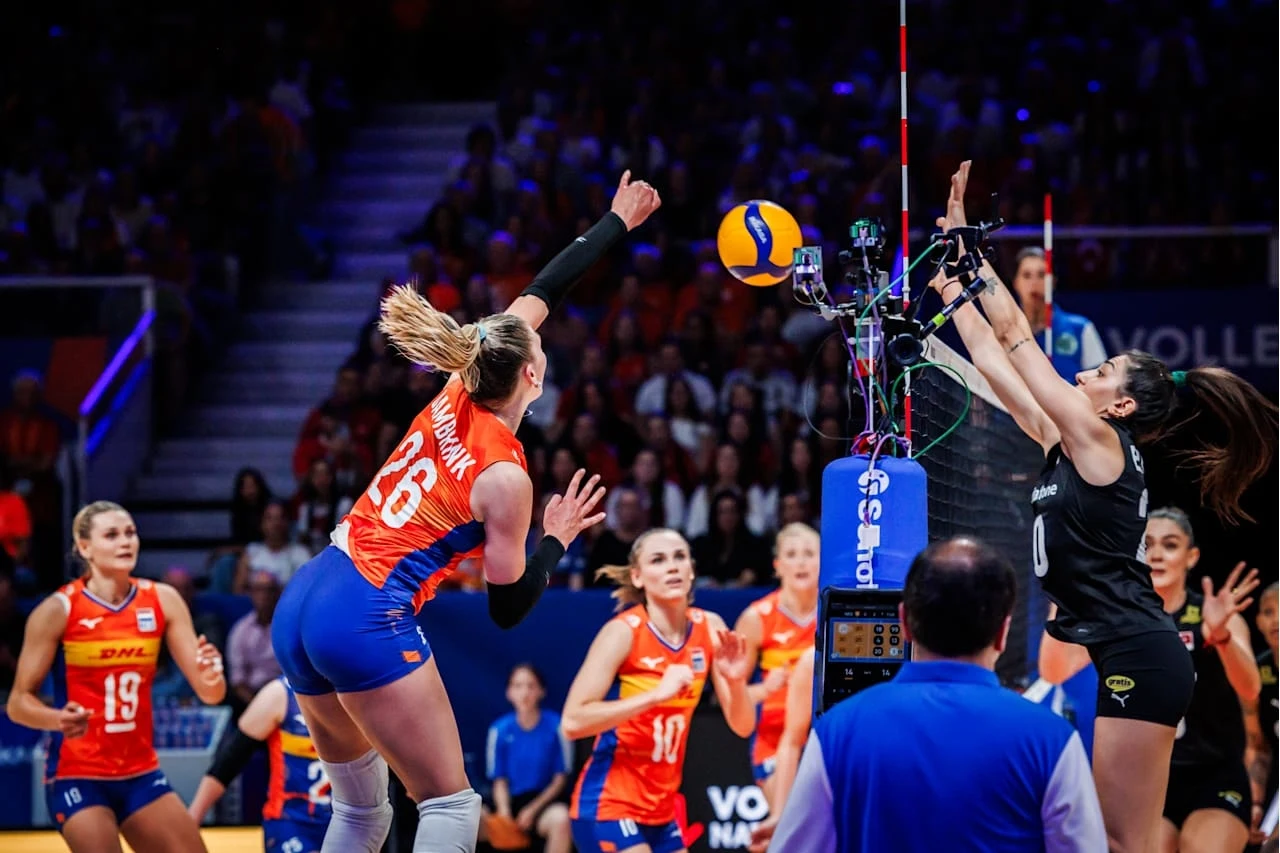 Zawodniczki dwóch drużyn siatkarskich walczą o piłkę przy siatce na hali sportowej, widownie w tle, dynamiczna akcja, koncentracja uczestniczek.