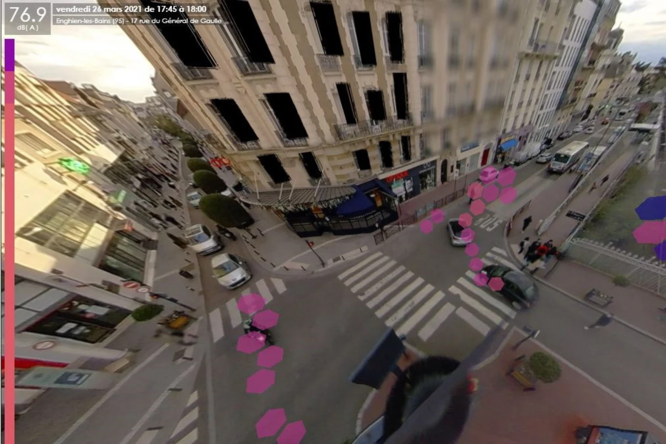 Panorama skrzyżowania miejskiego z pasami dla pieszych, otoczona wysokimi, jasnymi budynkami oraz samochodami zaparkowanymi przy ulicy, na obrazie widoczne są różowe punkty symbolizujące analizę ruchu pieszych.