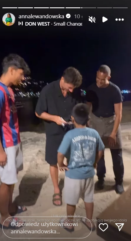 Robert Lewandowski rozdający autografy Czterech mężczyzn, w tym dwójka dorosłych i dwójka dzieci, stoi razem na plaży nocą, jedna z osób skupia się na przedmiocie trzymanym w rękach, pozostali obserwują.