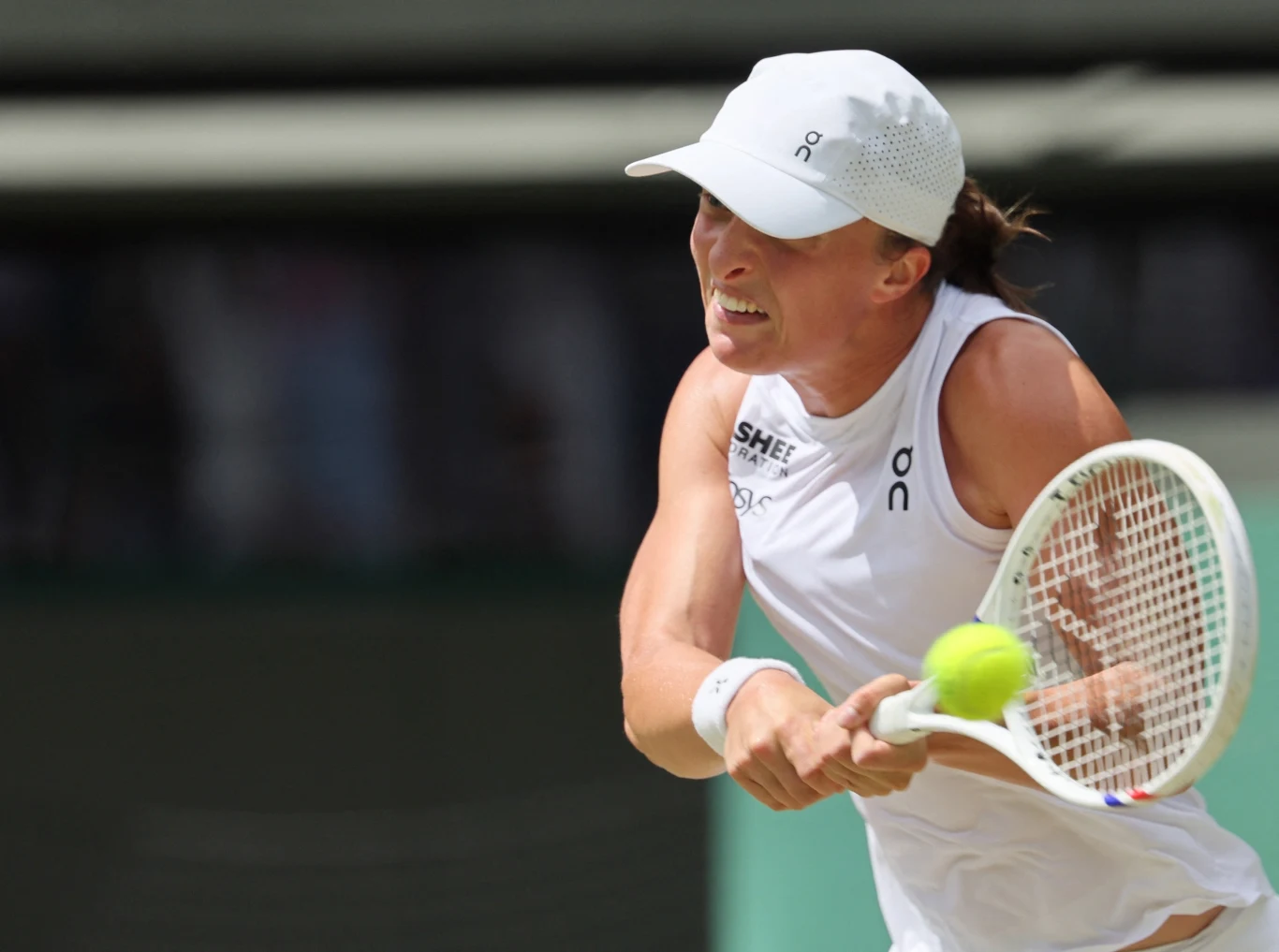 Zawodniczka podczas dynamicznej akcji tenisowej, skoncentrowana na uderzeniu piłki rakietą, ubrana w biały strój sportowy i czapkę z daszkiem na tle kortu.