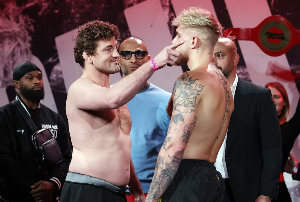 Ben Askren podczas ważenia przed walką z Jackiem Paulem Dwóch mężczyzn stoi naprzeciwko siebie, jeden z nich dotyka palcem twarzy drugiego, wokół nich kilku obserwatorów; atmosfera przypomina tradycyjne ważenie przed walką sportową.