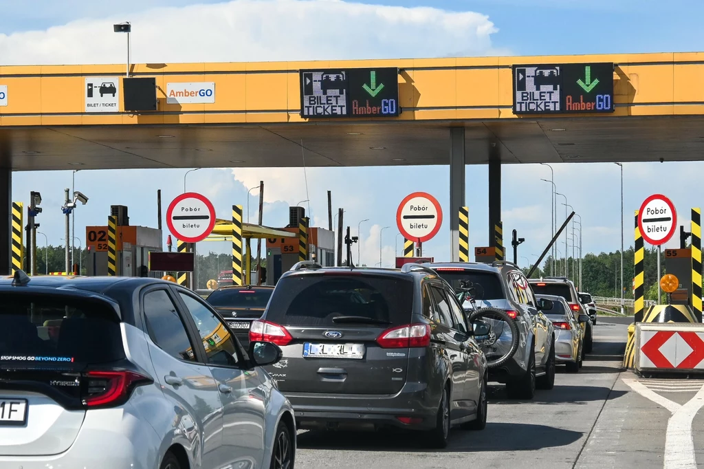 Płatności na autostradzie A1 można uiszczać na dwa różne sposoby. Samochody stojące w kolejce do punktu poboru opłat na autostradzie, widoczne bramki, znaki drogowe oraz barierki oddzielające poszczególne pasy ruchu.