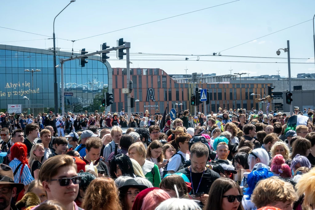 Podczas Pyrkonu miasto przeżywa prawdziwe oblężenie Tłum ludzi zgromadzony na ulicy w centrum miasta, wiele osób przebranych w kolorowe stroje cosplay, w tle nowoczesne budynki i oznaczenia drogowe, które podkreślają miejski charakter miejsca.